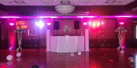 A dance floor with a white DJ booth, black speakers, and colorful stage lighting in a ballroom.