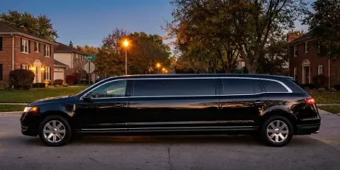 A black stretch limousine parked on a residential street at dusk.