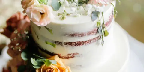 A two-tier semi-naked wedding cake decorated with fresh pink and yellow roses and greenery.