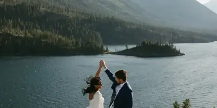 A bride and groom dancing on a rocky outcrop overlooking a mountain lake.