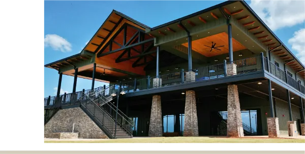 Exterior view of the Oakfuskee Conservation Center building featuring a large wooden overhang, stone pillars, and a staircase leading to the entrance.