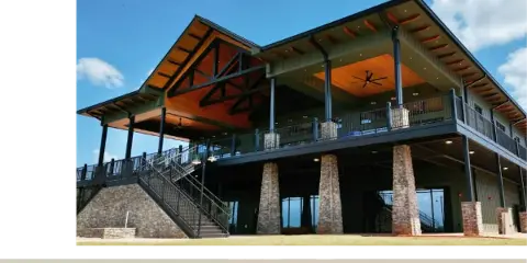 Exterior view of the Oakfuskee Conservation Center building featuring a large wooden overhang, stone pillars, and a staircase leading to the entrance.