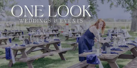 A wedding planner in a blue dress arranging table settings at an outdoor event.