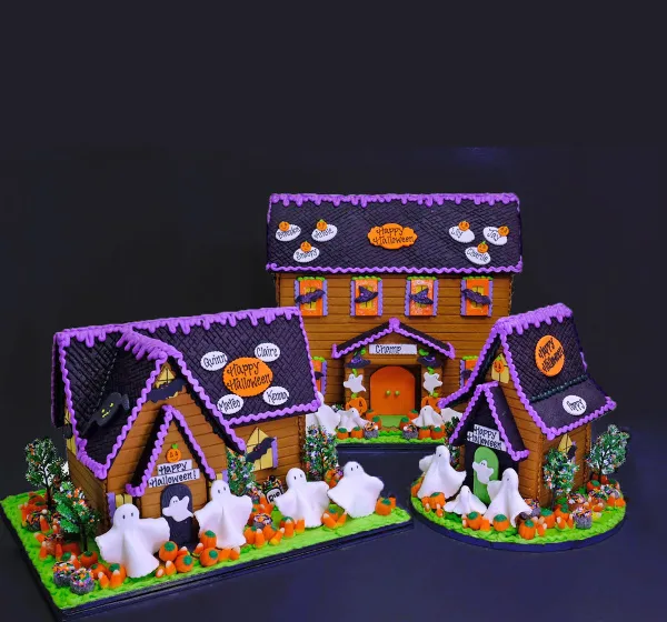 A custom Halloween-themed gingerbread house featuring purple icing, white fondant ghosts, and candy decorations.