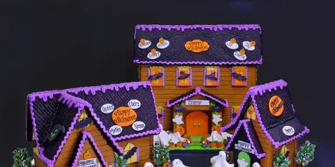 A custom Halloween-themed gingerbread house featuring purple icing, white fondant ghosts, and candy decorations.