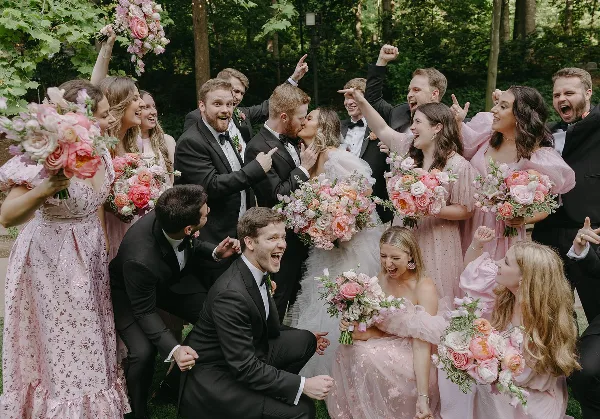 A wedding party including the bride and groom posing outdoors with pink floral bouquets.