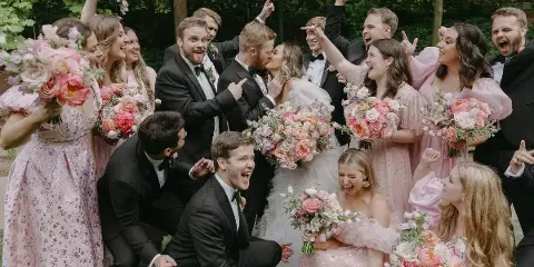 A wedding party including the bride and groom posing outdoors with pink floral bouquets.