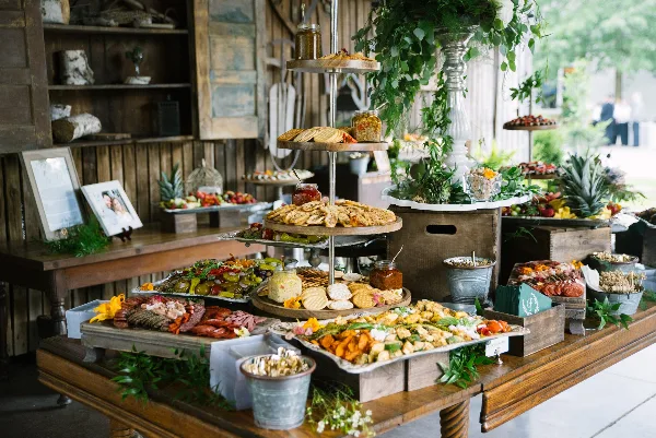A rustic catering table filled with a variety of appetizers, charcuterie, and a tiered cracker stand.