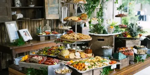 A rustic catering table filled with a variety of appetizers, charcuterie, and a tiered cracker stand.