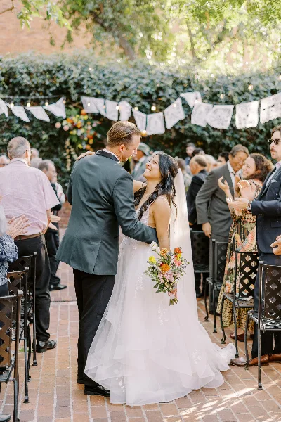 A bride and groom sharing a moment during an outdoor wedding ceremony with guests seated in the background.