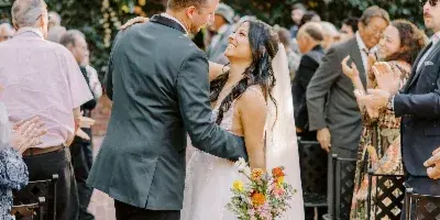 A bride and groom sharing a moment during an outdoor wedding ceremony with guests seated in the background.