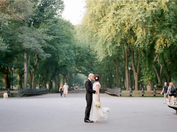 A bride and groom standing in a park with trees in the background.