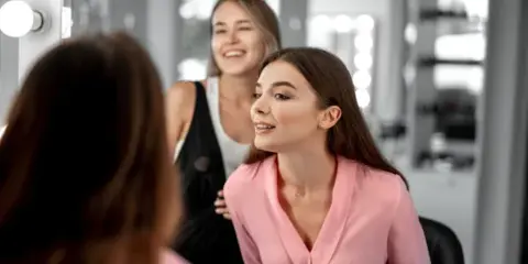 A professional beauty artist working on a client's hair and makeup in a studio setting.