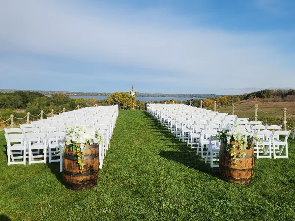 Rows of white folding chairs arranged on a grassy lawn with barrel planters for an outdoor wedding ceremony.