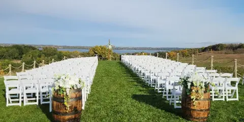 Rows of white folding chairs arranged on a grassy lawn with barrel planters for an outdoor wedding ceremony.