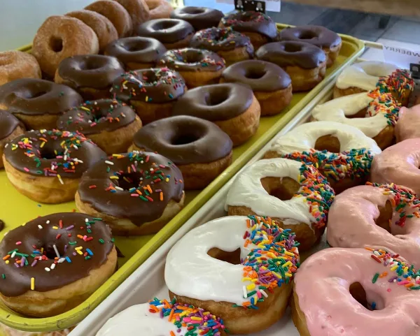 A close-up view of trays filled with chocolate, white, and pink frosted donuts topped with colorful sprinkles.