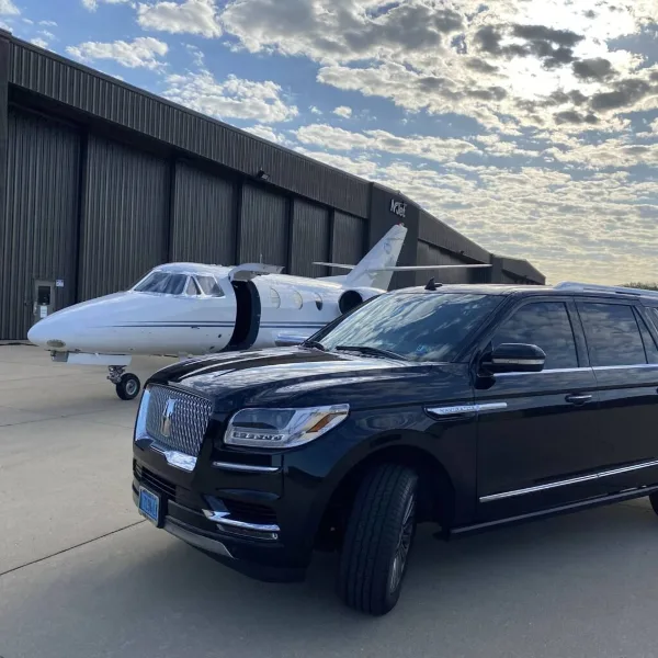 Black luxury SUV parked in front of a private jet at an airport hangar.
