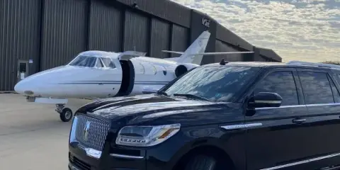 Black luxury SUV parked in front of a private jet at an airport hangar.