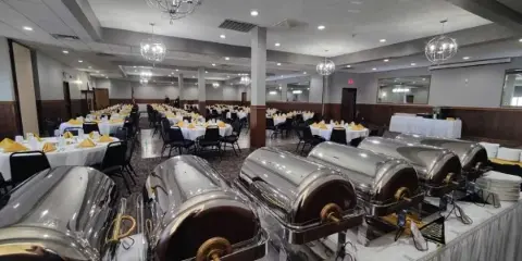 A banquet hall set up for an event with round tables and a row of stainless steel chafing dishes in the foreground.