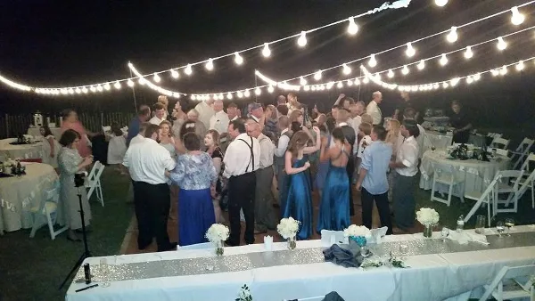 A crowded wedding reception at night with guests dancing under string lights.