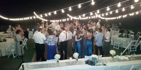 A crowded wedding reception at night with guests dancing under string lights.