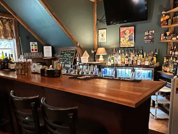 Interior view of a wooden bar counter with shelves of liquor bottles, glassware, and bar equipment in a lodge setting.