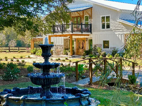 Exterior view of The Grove Estate wedding venue featuring a large fountain in the foreground and a two-story building with a balcony and stone accents.