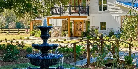Exterior view of The Grove Estate wedding venue featuring a large fountain in the foreground and a two-story building with a balcony and stone accents.