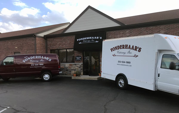 Exterior of Vonderhaar's Catering building with a branded maroon van and white delivery truck parked in front.