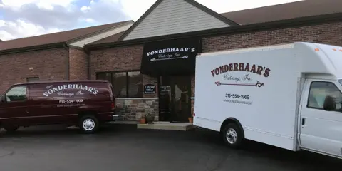 Exterior of Vonderhaar's Catering building with a branded maroon van and white delivery truck parked in front.