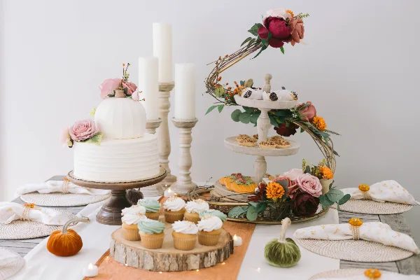 A wedding dessert table featuring a white tiered cake with floral decorations, a stand of assorted pastries, and a wooden board of cupcakes.