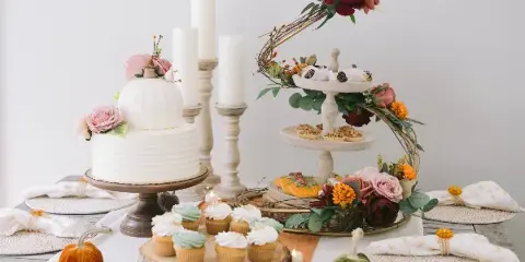A wedding dessert table featuring a white tiered cake with floral decorations, a stand of assorted pastries, and a wooden board of cupcakes.