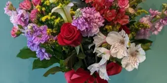 A colorful floral arrangement featuring roses, calla lilies, and alstroemeria in a glass vase with a red ribbon.