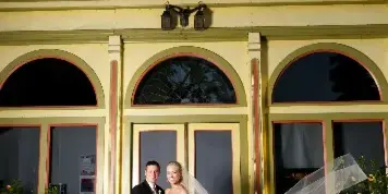 Bride and groom posing in front of the Yellow Tavern building with the bride’s veil blowing in the wind.