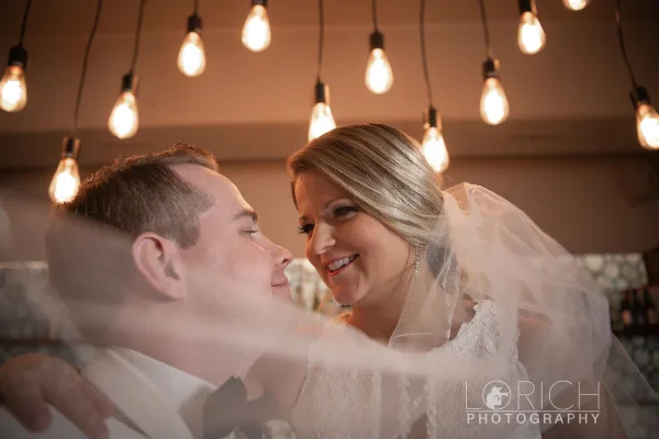 A bride and groom sharing a moment during a wedding reception under hanging string lights.