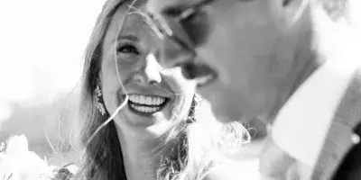 A black and white photograph of a smiling bride and groom at a wedding.