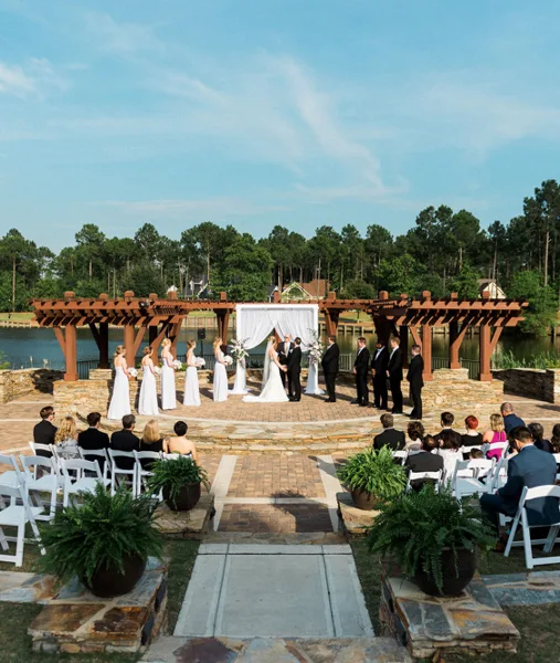 Outdoor wedding ceremony with bride and groom at an altar, surrounded by wedding party and seated guests.