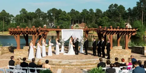 Outdoor wedding ceremony with bride and groom at an altar, surrounded by wedding party and seated guests.