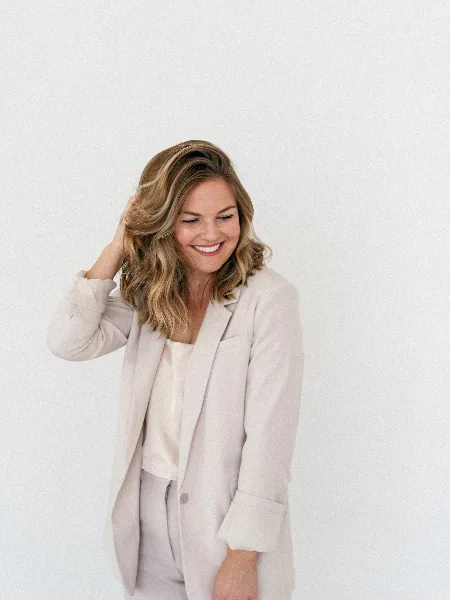 Portrait of a smiling woman with blonde hair wearing a light-colored blazer and trousers.