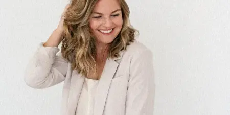 Portrait of a smiling woman with blonde hair wearing a light-colored blazer and trousers.