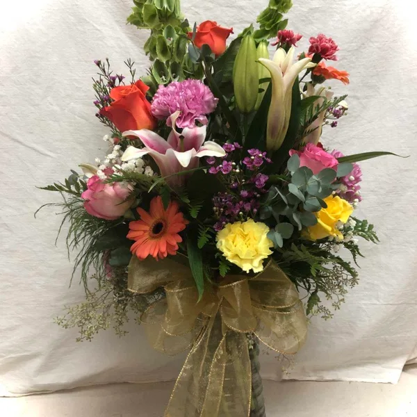 A mixed floral bouquet in a glass vase featuring lilies, roses, and gerbera daisies.