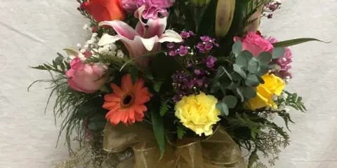 A mixed floral bouquet in a glass vase featuring lilies, roses, and gerbera daisies.