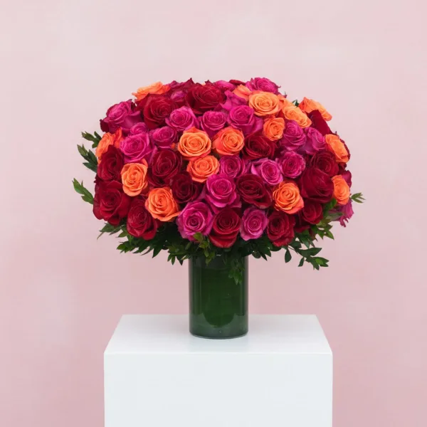 A round bouquet of red, pink, and orange roses in a green glass vase.