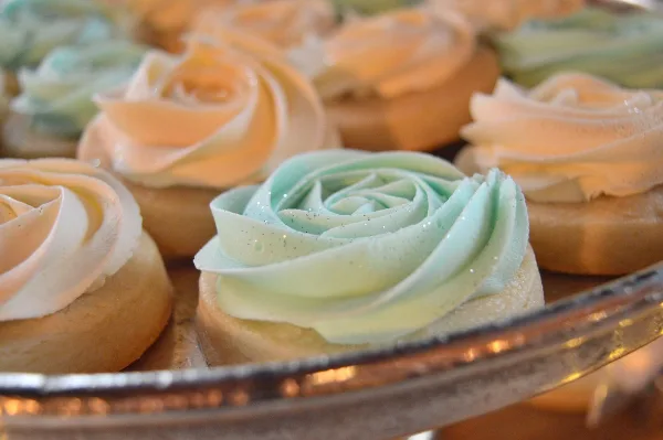 Close-up of custom frosted desserts with rose-style icing in pastel colors on a display stand.