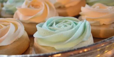 Close-up of custom frosted desserts with rose-style icing in pastel colors on a display stand.