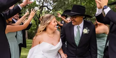 A bride and groom walking hand-in-hand through an outdoor venue surrounded by guests.