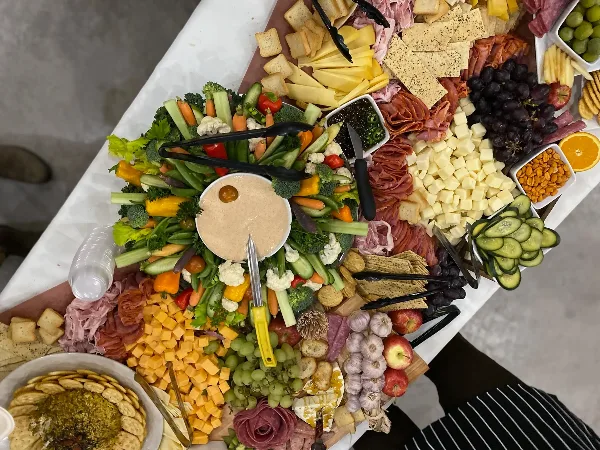 Overhead view of a catering grazing table filled with assorted meats, cheeses, fresh vegetables, grapes, crackers, and a central dip.