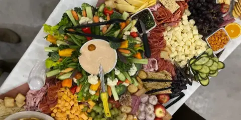 Overhead view of a catering grazing table filled with assorted meats, cheeses, fresh vegetables, grapes, crackers, and a central dip.