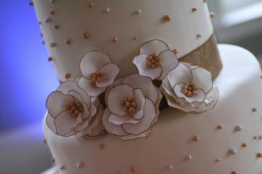 A close-up of a white wedding cake tier decorated with white sugar flowers and a burlap ribbon.