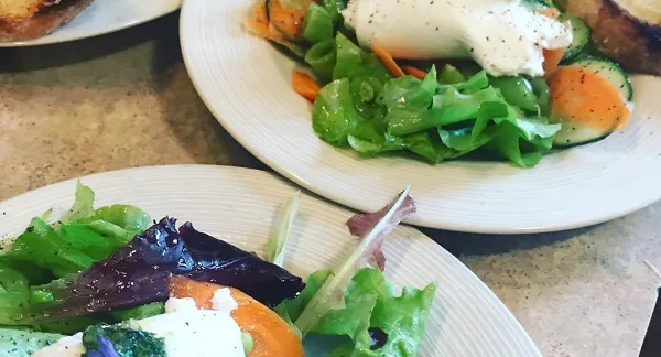 A close-up of a plated gourmet salad featuring mixed greens, burrata cheese, and fresh vegetables.